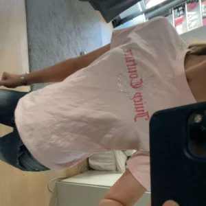 Ljusrosa t-shirt från Juicy Couture - Säljer en ljusrosa t-shirt från Juicy Couture med glittrig logga och text i rött framtill. T-shirten har rund halsringning och korta ärmar. Perfekt för en avslappnad och trendig look.