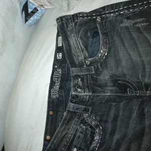 Miss me pant - Säljer ett par svarta jeansbyxor från Miss Me med dekorativa sömmar och detaljerade bakfickor. Byxorna har normal passform och klassisk femficksdesign med snygga nitar och knappar. Perfekta för dig som gillar unika detaljer på jeans.