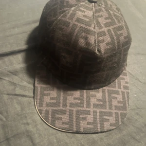 Svart Fendi keps  - Säljer en svart keps från Fendi med det klassiska FF-mönstret över hela kepsen. Kepsen har böjd skärm och justerbar passform baktill. Perfekt accessoar för en trendig streetwear-look. Tar även emot byten med andra kepsar 