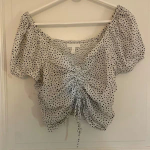 Vit prickig croppad blus från H&M - Supersöt vit blus med svarta prickar från H&M. Modellen är croppad med korta puffärmar och knytning framtill som ger en snygg rynkad effekt. Perfekt för en trendig och somrig look. Speciellt nu när de prickiga mönstret är trendigt 💖