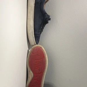 Mörkblå sneakers med röd sula - Snygga mörkblå sneakers med vit sula och röd undersida. Skorna har snörning och en klassisk rund tå. Ovandelen är i mocka och insidan är ljusbeige. Perfekta för dig som vill ha en stilren och bekväm sko till vardags.     priset är inte hugget i Sten