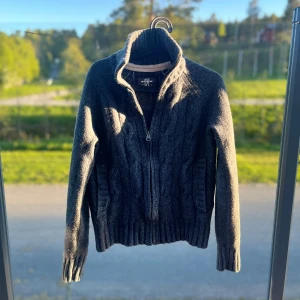 Helzip stickad mörkgrå  - Mysig mörkgrå stickad kofta från L.O.G.G. med hög krage och dragkedja framtill. Tröjan har långa ärmar, ribbade muddar och två fickor framtill. Perfekt för kyliga dagar. 8/10 skick