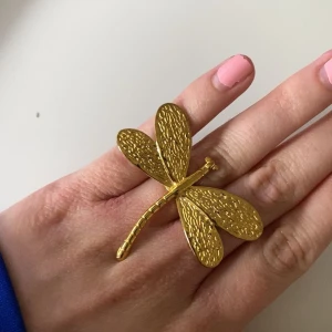 Stor guldfärgad ring med trollslända - Unik och iögonfallande ring i form av en stor trollslända i guldfärgad metall. Ringen har fina detaljerade vingar och passar perfekt för dig som vill sticka ut med ditt smycke.