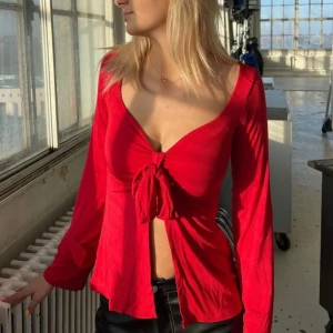 Röd långärmad topp med knyt från Design by Si - Trendig röd topp från Design by Si med lång ärm och snygg knytning framtill. Djup v-ringning och figurnära passform som ger en modern look. Perfekt att styla med jeans eller kjol. Använd två gånger, pris kan diskuteras🤗