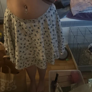 Vit blommig kjol från SHEIN - Säljer en söt vit kjol från SHEIN med blått blommönster. Kjolen har en luftig och svängande passform med resår i midjan och volangdetalj. Perfekt för dig som gillar en feminin och somrig stil!