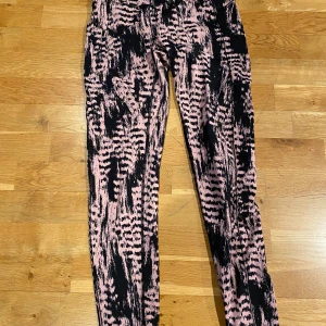 Rosa och svarta leggings med abstrakt mönster - Säljer ett par Casall tights i rosa och svart med ett coolt abstrakt mönster. Byxorna har en tight passform och är perfekta för dig som vill sticka ut lite extra. Superstretchigt material som sitter skönt hela dagen. Stl 38