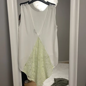 Vit ärmlös topp med spetsdetalj från Tally Weijl - Säljer en vit ärmlös topp från Tally Weijl med v-ringning och ljusgul spetsdetalj framtill. Toppen har en lös passform och är tillverkad i ett lätt, syntetiskt material. Perfekt för varma dagar, storlek M/L. Hör av er 💗