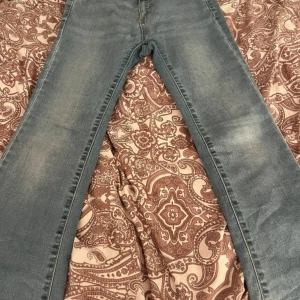 Blå jeansbyxor i klassisk modell - Säljer ett par blå jeansbyxor i klassisk modell. Byxorna har normal passform och är tillverkade i denim med ljusa slitningar framtill och bakfickor. Perfekta för en avslappnad stil.