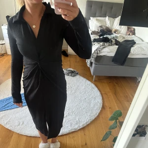 Svart långärmad klänning med krage - Säljer en svart långärmad klänning med krage och v-ringning. Klänningen har en twistad detalj i midjan som ger en snygg siluett och är i en figurnära modell. Klänningen är varsamt använt och om man kollar nära är den lite lite knottrig men inget man ser på normalt avstånd. Den är från Gina tricot och är storlek S