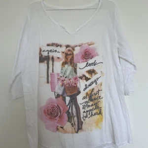 Vit långärmad topp med tryck av tjej och rosor - Vit långärmad topp med v-ringning och tryck framtill av en tjej med cykel, rosa rosor och text. Tunt och mjukt material, perfekt för en avslappnad stil. Trekvartsärm och lös passform.