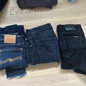 Tre par svarta och mörkblå jeans - Säljer tre par jeans i svart och mörkblått. Ett par från Nudie Jeans med klassiska kontrastsömmar och rå kant nertill, ett par svarta jeans med enkel design och ett par svarta jeans från Nudie med läderpatch bak. Perfekta till vardags!