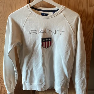 Vit sweatshirt från GANT med broderad logga - Säljer en vit sweatshirt från GANT med logga och sköld på bröstet. Tröjan har långa ärmar. Klassisk och stilren modell som passar till mycket.