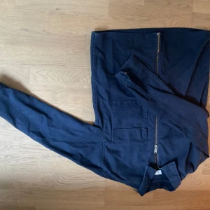 Mörkblå overshirt med dragkedja - Säljer en mörkblå overshirt med dragkedja och stora fickor framtill. Jackan har klassisk krage och är långärmad, perfekt för lager-på-lager. Enkel och stilren design som passar till det mesta.