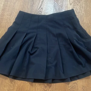 Svart plisserad kjol från H&M Divided - Säljer en svart plisserad kortkjol från H&M Divided. Kjolen har en klassisk A-linjeform och är perfekt för dig som gillar en stilren och enkel look. Passar till många olika outfits och är lätt att matcha.