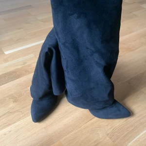 Svarta höga stövlar med klack - Säljer ett par svarta höga stövlar i mocka med spetsig tå och klack. Stövlarna har dragkedja på insidan och en elegant, slouchy passform. Perfekta för att lyfta vilken outfit som helst. Obs aldrig använda.