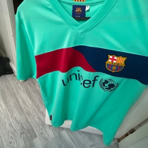 FC Barcelona Messi 10 fotbollströja - Säljer en mintgrön FC Barcelona fotbollströja med Messi 10 på ryggen. Tröjan har klubbmärke på bröstet, UNICEF-tryck och ett rött och mörkblått band över bröstet. Officiell produkt med korta ärmar och V-ringning.