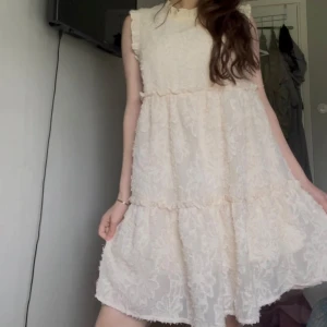 volangklänning från By Swan - Supersöt ljus klänning från By Swan med volangdetaljer och strukturmönster. Klänningen är ärmlös och har en lös passform med romantiska volanger längs axlar och kjol. Perfekt för sommarens alla tillfällen!