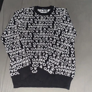 Svartvit tröja från Dolce & Gabbana - Cool svart tröja med vit Dolce & Gabbana-logga tryckt över hela plagget. Tröjan har rund halsringning och ribbade muddar vid ärmslut och nederkant. Perfekt statement piece för dig som gillar designerplagg.