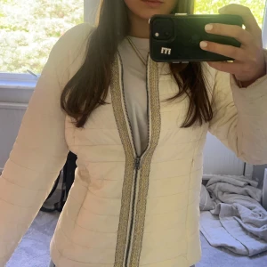 Vit jacka - Beige/vit jacka med detaljer längs dragkedjan. Ganska tunn.