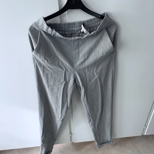 Grå byxor från Vero Moda - Gråa byxor från Vero Moda med elastisk midja och raka ben. Byxorna har fickor fram och dekorativa fickor bak. Perfekta för en stilren och bekväm look.
