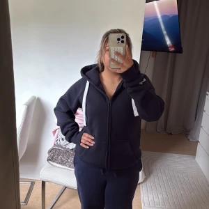 Mörkblå hoodie med dragkedja från Russemerch  - Säljer en mörkblå hoodie från Russemerch med vita snören i huvan. Tröjan har fickor framtill och tryckt logga på ärmen. Perfekt för dig som vill ha en enkel och stilren hoodie. Fick hem den idag och säljer den då den är för stor så helt oanvänd med prislapp kvar.