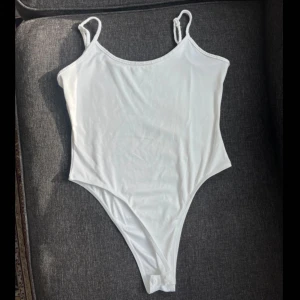 Vit bodysuit med smala axelband - Säljer en enkel och stilren vit bodysuit med smala axelband och justerbara. Perfekt att styla till jeans eller kjol för en clean look. Mjuk och stretchig känsla. Helt ny!