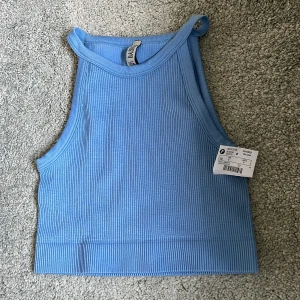 Ljusblå linnetopp - Säljer en ljusblå ribbad linnetopp från Basics. Toppen har en croppad passform och är ärmlös med hög halsringning. Perfekt för varma dagar eller som lager under en skjorta. Materialet är mjukt och stretchigt.💕