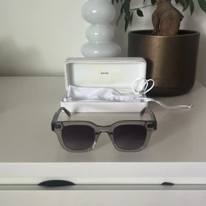 Grå transparenta solglasögon från CHIMI - Säljer ett par stilrena solglasögon från CHIMI i transparent grå plast med fyrkantig form. Glasögonen har mörka linser. Perfekt accessoar för att lyfta din look.