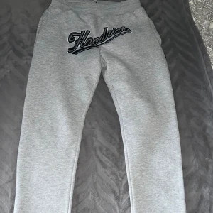 Grå mjukisbyxor med tryck - Säljer ett par grå mjukisbyxor med svart och vitt tryck framtill där det står 'Hoodies' och ett mindre tryck bak på fickan med texten 'Hoop Series'. Byxorna har en avslappnad passform och är perfekta för chill dagar.