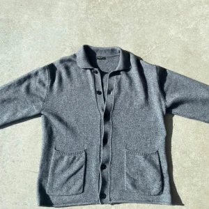Grå kofta från Massimo Dutti - Mysig grå kofta från Massimo Dutti med knappar framtill och två stora fickor. Klassisk krage och ribbade detaljer vid ärmslut och krage. Perfekt för lager-på-lager och enkel att matcha med olika outfits. Köpt i Hamburg i deras egna butik. Nypris 850 kr. Tröjan är knappt använd. Tröjan är i storlek L men rekommenderar om du är S-M. Går inte att hitta i svenska butiker. Kvitto finns.