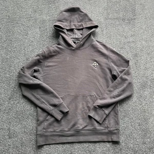 Svart hoodie från J.Lindeberg - Säljer en stilren svart hoodie från J.Lindeberg med logotyp på bröstet. Tröjan har huva, magficka och långa ärmar. Perfekt för en avslappnad look och enkel att matcha med andra plagg.