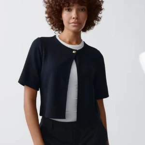 Svart kortärmad kofta med knapp - Säljer en svart, kortärmad kofta med en dekorativ knapp framtill. Koftan är croppad och har en stilren, enkel design som passar perfekt över en topp eller klänning.