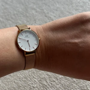 Guldig klocka från Daniel Wellington - Säljer en stilren klocka från Daniel Wellington med guldig mesh-länk och vit urtavla. Klockan har minimalistisk design och DW-logga på spännet. Perfekt accessoar för dig som gillar klassisk och elegant stil. Behöver ny batteri. Går att byta i varje klockaffär. Därför är priset så billigt. 
