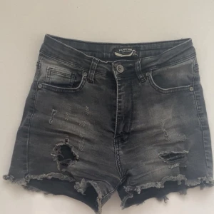 Svarta jeansshorts - Snygga svarta jeansshorts från Happy Pink med slitna detaljer och fransig kant nedtill. Högmidjade modell med klassiska fickor fram och bak. Perfekta för en cool och avslappnad stil.