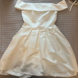 Vit offshoulder klänning i satin - Superfin vit klänning med offshoulder och utsvängd nedtill, och har endast används en gång på skolavslutningen. Gjord i glansigt satinmaterial som ger en lyxig känsla. Perfekt för speciella tillfällen när du vill sticka ut. Kjolen har fina veck och klänningen är axelbandslös. Köptes för 899kr, men pris kan diskuteras😊😊