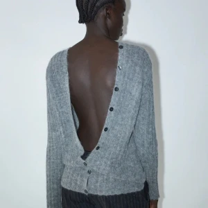 Grå stickad kofta från Paloma Wool - Säljer en grå stickad kofta från Paloma Wool med djup öppen rygg och knappar längs ryggen. Koftan har lång ärm och är tillverkad i ett mjukt, fluffigt material! Helt oanvänd! Köpt för 180€