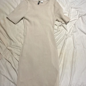 Beige ribbad kortklänning från H&M - Säljer en beige ribbad kortklänning från H&M med rund halsringning och korta ärmar. Klänningen har en tight passform och är perfekt för dig som gillar en enkel och stilren look.