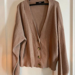 Beige ribbad kofta från BikBok - Säljer en beige ribbad kofta från BikBok i storlek S. Koftan har v-ringning, långa ärmar och stora knappar framtill. Perfekt att slänga på sig över en topp för en avslappnad look.