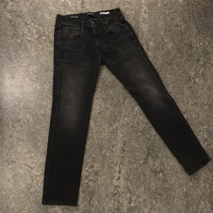 Svarta Replay Hyperflex Anbass jeans - Säljer ett par svarta Replay Hyperflex Anbass jeans med klassisk femficksdesign och diskreta slitningar. Jeansen har normal passform och raka ben, tillverkade i stretchigt material för extra komfort. Perfekta för dig som gillar stilrena och bekväma jeans.