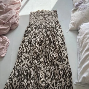 Populär Zara kjol - Säljer en svartvit långkjol med grafiskt mönster och smock i midjan. Kjolen har en luftig och flowy passform, perfekt för varma dagar. Tyget är mjukt och bekvämt, och midjan är elastisk för extra komfort.