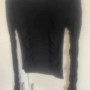 Svart långärmad topp från BikBok - Säljer en svart långärmad topp från BikBok i storlek S. Toppen har rynkade detaljer längs ärmarna och sidorna, vilket ger en snygg och trendig look. Perfekt att styla till olika outfits!