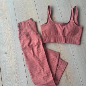 Rosa ribbade träningstights från Aim'n - Säljer ett par snygga ribbade träningstights från Aim'n i en dämpad rosa färg. Tightsen har hög midja och är gjorda i ett stretchigt material som sitter skönt på kroppen. Perfekta för gymmet eller yoga!Pink beat ribbed set från AIM’N. Nyskick-mycket fint skick. Skickas i förpackning.  Tights: XS  Top S