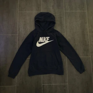 Marinblå hoodie från Nike - Säljer en marinblå hoodie från Nike med vit logga på bröstet. Tröjan har huva med dragsko och en magficka. Använd ett fåtal gånger och inga defekter. Säljer då den är lite för stor för mig😽❤️