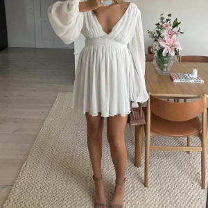 Studentklänning/Vit omlottklänning från NA-KD - Superfin vit omlottklänning från NA-KD med lång ärm och markerad midja. Klänningen har v-ringning, lätt plisserat tyg och flowig kjol. Perfekt för sommarens tillfällen och studentfirande. Den är helt oanvänd med prislapp kvar. Köpte den för 899kr säljer för 749kr. Den är i storlek 44 men skulle passa en som är 42