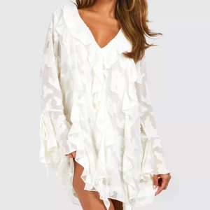 Vit volangklänning med v-ringning - Säljer en luftig vit klänning med v-ringad hals och volangdetaljer. Klänningen har lång ärm och ett subtilt blommigt mönster i tyget. Perfekt för sommarens tillfällen och har en romantisk känsla.