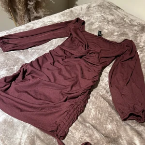Vinröd klänning med långa ärmar - Snygg vinröd klänning med långa ärmar och v-ringad design. Klänningen har en knytning i midjan och är gjord i ett mjukt material. Perfekt för en stilren look.