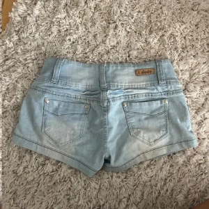 Ljusblå jeansshorts från i dodo - Snygga ljusblå jeansshorts från i dodo med låg midja och knappar framtill. Perfekta för sommardagar eller till en stickad tröja. Säljer då dem är lite små på mig🩷🩷