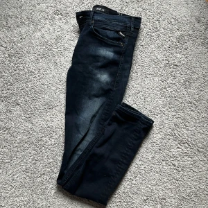 Replay jeans - Snygga mörkblå jeans från Replay i modellen Anbass. De har en klassisk femficksdesign och en stilren look. Perfekta för en avslappnad stil med en touch av elegans. Midjan är märkt med storlek 31.