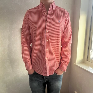 Randig Ralph lauren skjorta - Säljer nu en riktigt snygg, röd-vitrandig Ralph lauren skjorta i strl M🔥Skjortan är i riktigt bra skick, helt oanvänd och som ny, ‼️10/10‼️Riktigt snygg nu till sommaren!☀️Nypris: ca 1700kr, mitt pris: 329kr! Svarar på alla frågor o svarar snabbt!📝