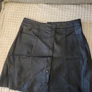 Svart kjol från Divided - Snygg svart kjol från Divided i skinnimitation med knappar framtill. Perfekt för en trendig look. 🖤